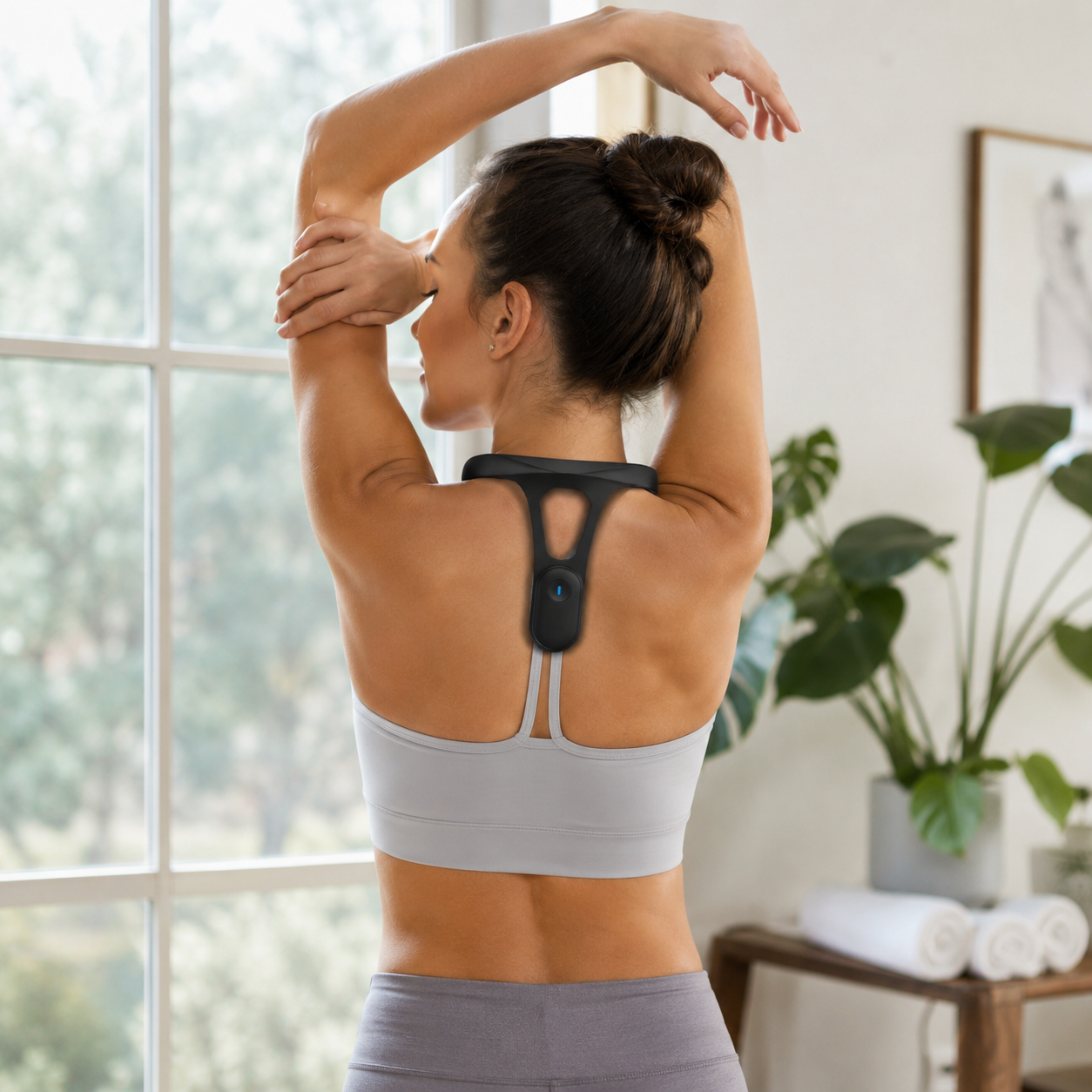 Woman stretching at a window wearing the black AlignPulse trainer between the shoulder blades
